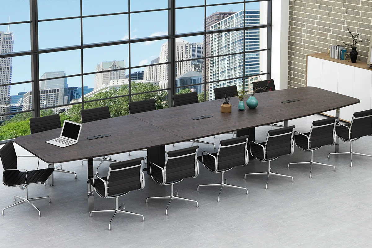 Long conference table with multiple black leather chairs in a bright office, overlooking a city skyline through large grid windows; a laptop sits on the table.