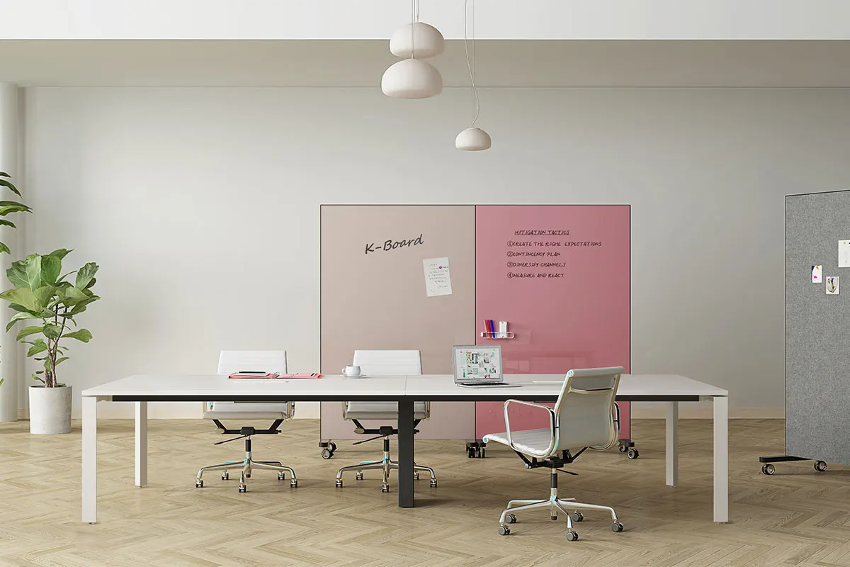 Modern office meeting room with a long white table, white chairs, and a pink divider board; plant on the left and a gray cabinet on the right while a laptop sits on the table.