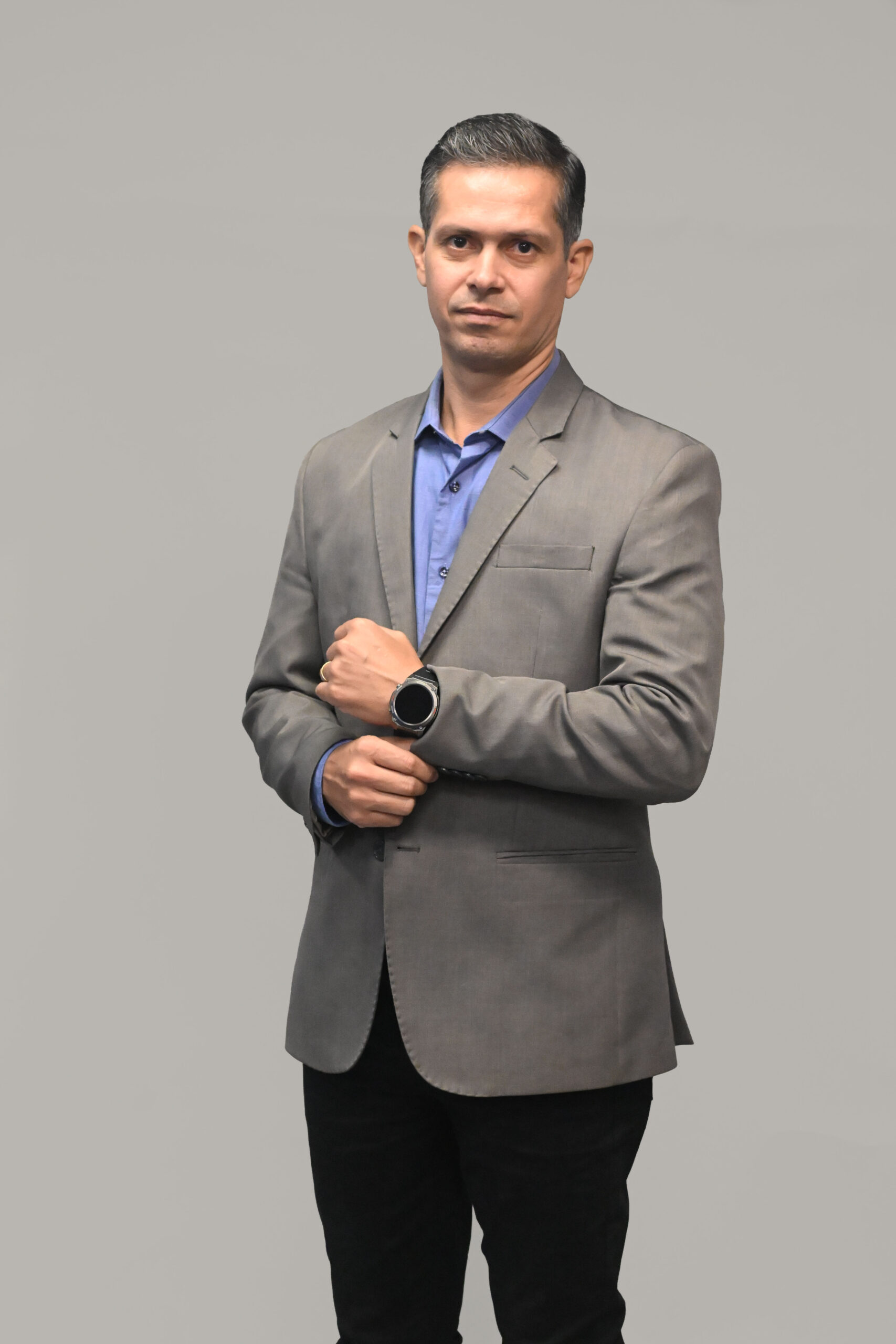 WESLEY DUARTE SUPORTE TÉCNICO GP CABLING | gpcablingcombr | gpcablingcombr Professional portrait of a man in a gray suit and blue shirt standing with hands clasped against a neutral gray background