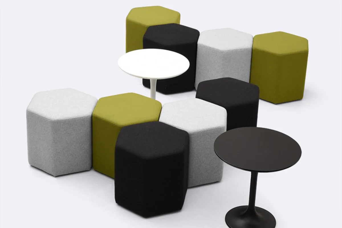 Modular hexagonal ottomans in gray, white, black, and olive surround two round tables (white and black) in a lounge setting.