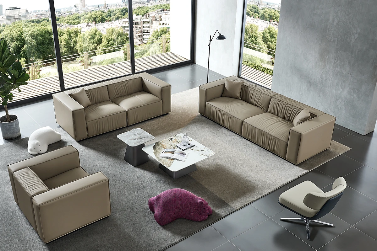 Open-plan living room with two beige leather sofas, a matching armchair, marble coffee tables, and a purple pouf on a gray rug near large windows overlooking the city.