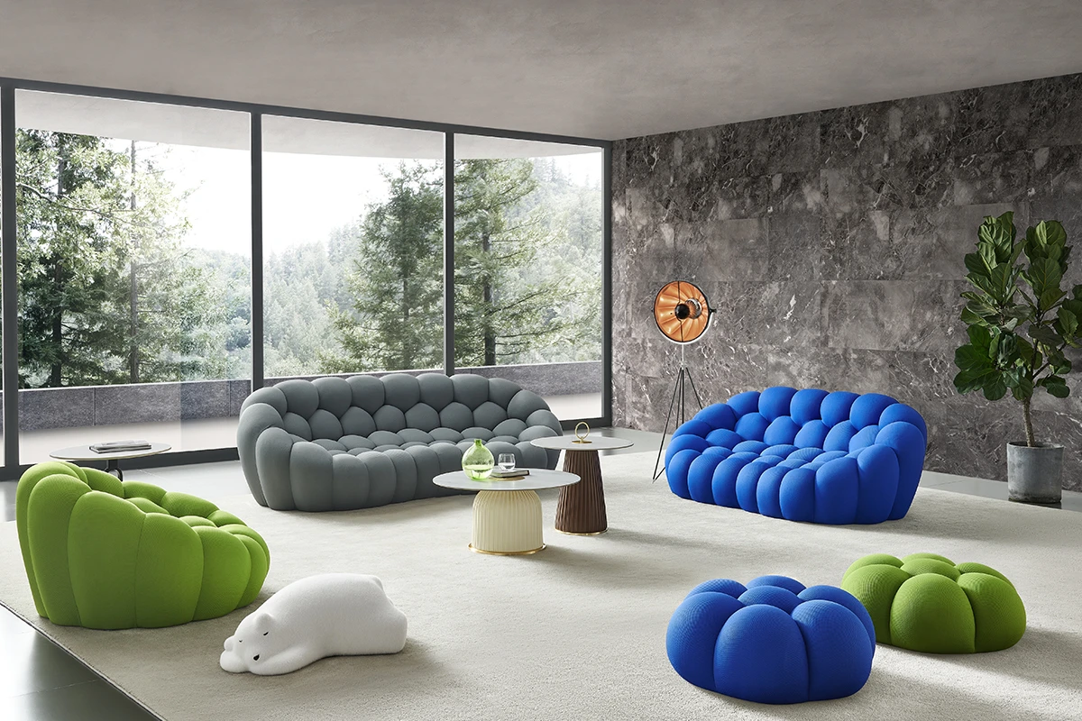 Modern living room with colorful bubble-style sofas in green, blue, and gray by large windows overlooking trees.