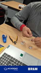 Person working with Ethernet cables at a desk, using wire strippers and a crimping tool with loose twisted-pair wires nearby on the table.