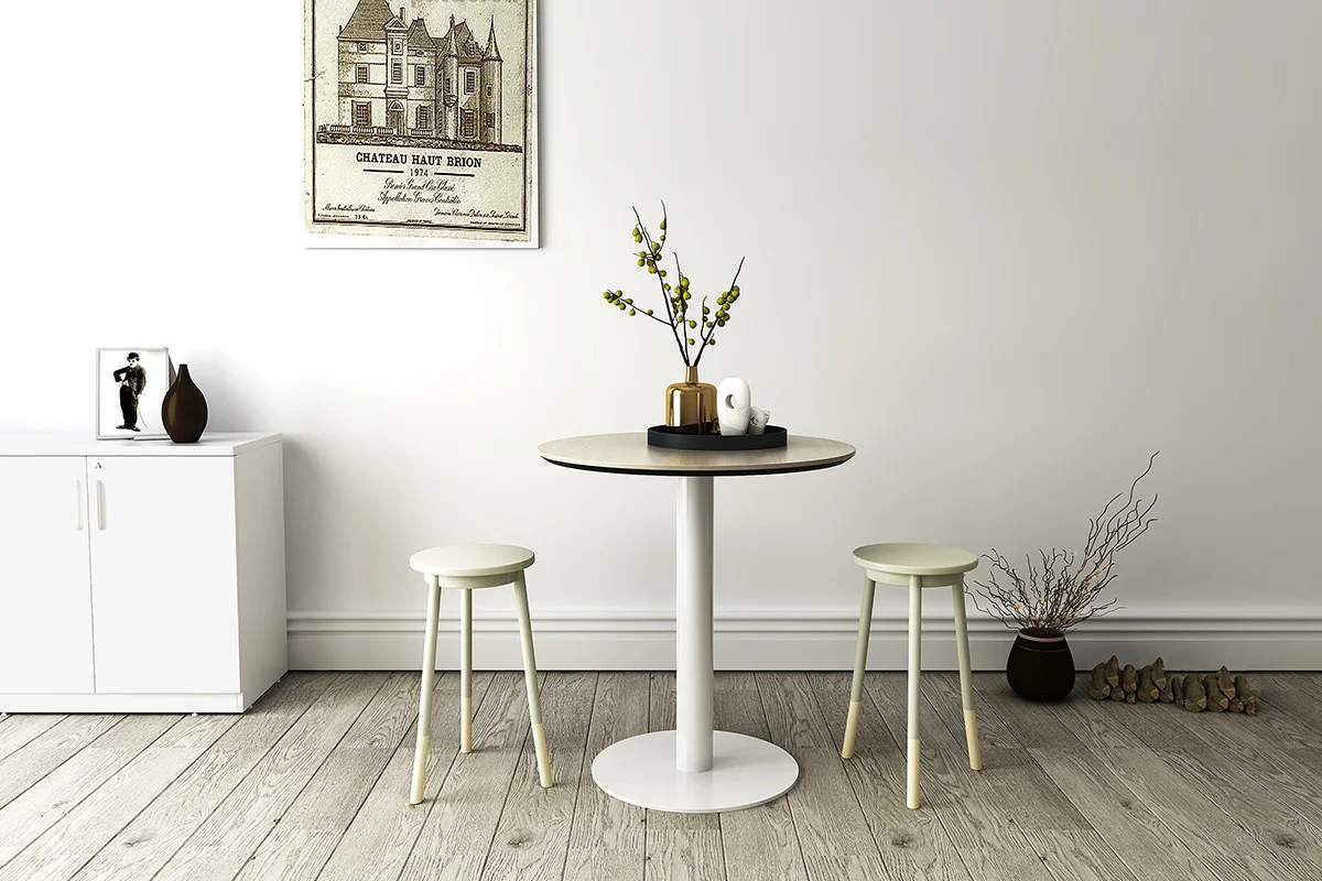 White round pedestal table with two light stools in a minimalist, neutral-toned room with a vase of branches and wall art above a white cabinet on the left.
