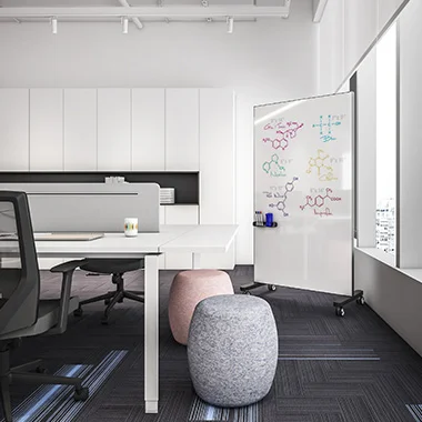 Modern office workspace with white desks and a movable whiteboard showing colorful molecular drawings, plus two gray poufs.