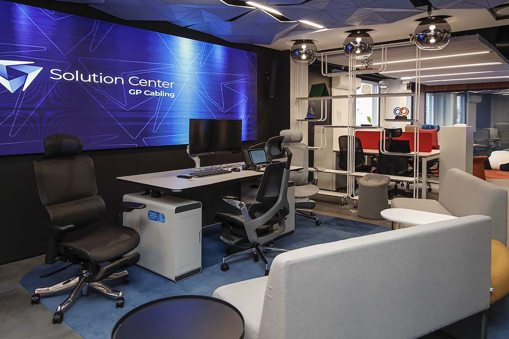 Modern office workspace with a blue branded wall reading 'Solution Center GP Cabling' and several desks and computers nearby.