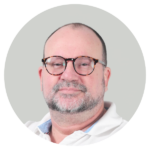 Close up portrait of a middle aged man with a beard and tortoiseshell glasses wearing a white collared shirt against a light gray background