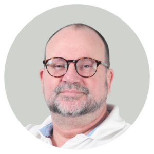 Close up portrait of a middle aged man with a beard and tortoiseshell glasses wearing a white collared shirt against a light gray background