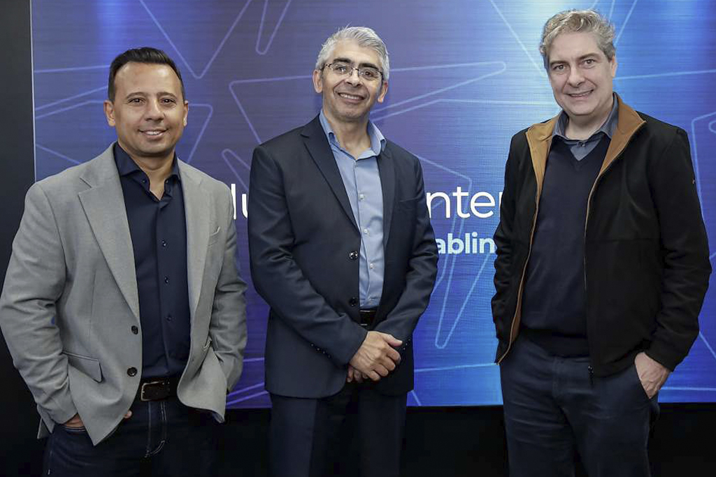 Three men in business attire pose for a photo against a blue technology backdrop, smiling.