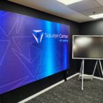 gp cabling solutoin center junho 2026 32 | gpcablingcombr Large blue digital display wall reading Solution Center with a freestanding monitor on a wheeled stand in a dark room