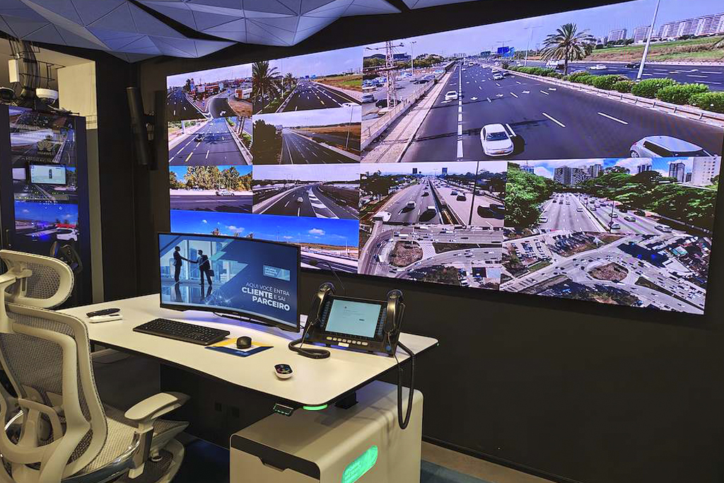 Control room with a large video wall displaying multiple city traffic feeds; desk has monitors, keyboard, and headset for operators.