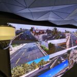 gp cabling solutoin center junho 2026 64 | gpcablingcombr Curved video wall showing a collage of highway scenes with cars and palm trees plus a security camera in the foreground under a geometric blue ceiling