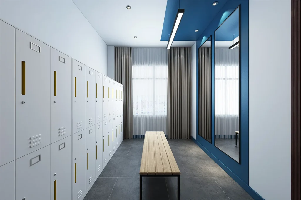 Locker room with a row of white lockers along the left wall a wooden bench in the center and blue framed mirrors on the right