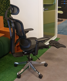 Ergonomic black office chair with adjustable armrests and a retractable footrest on a wheeled base in an office setting.