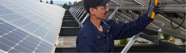Technician wearing safety glasses and a blue uniform installs solar panels on a rooftop