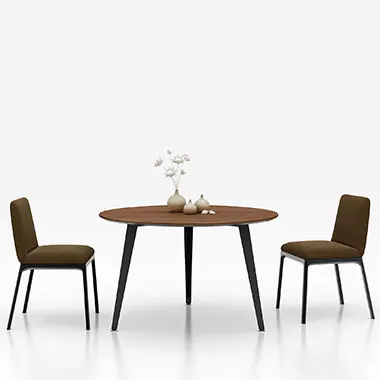 Round wooden dining table with two brown upholstered chairs on a white studio background; small vase of flowers at the center.