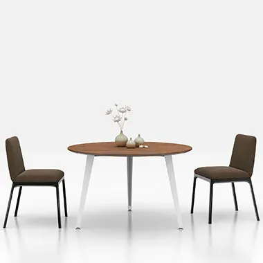 Round wooden dining table with two brown upholstered chairs in a minimal bright setting a small vase and decor on the table center