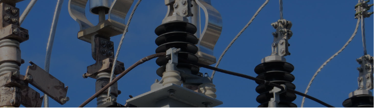 Close up of high voltage power lines and ceramic insulators on metal pylons against a bright blue sky