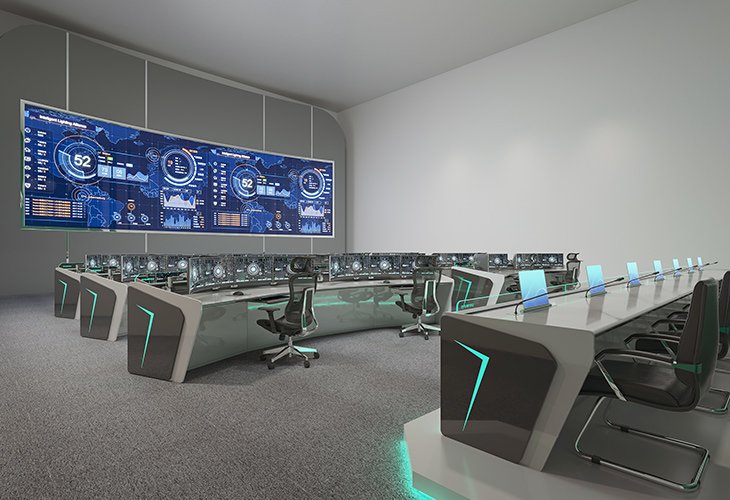 A futuristic command center with a long curved desk, numerous monitors, and a large wall of blue digital dashboards behind the workstations.