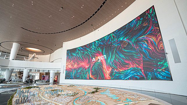 Spacious modern gallery with a large curved wall mural featuring swirling teal, pink, and purple patterns and a scale model display in the foreground
