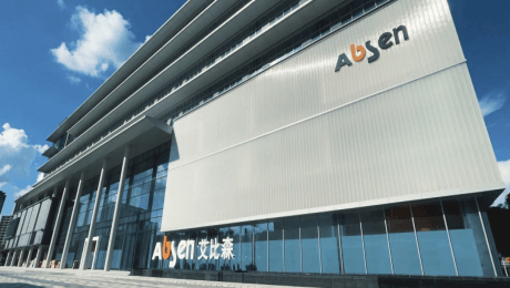 Modern glass-and-metal building with the AUSEN sign on the facade against a blue sky.
