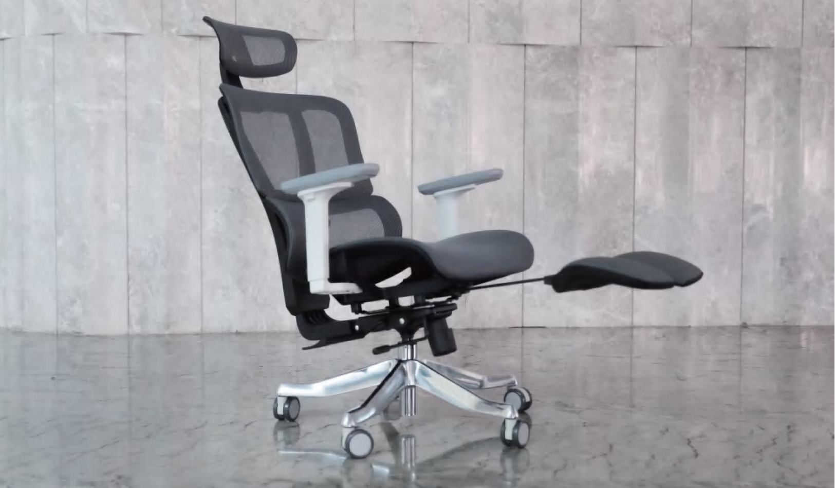 Ergonomic office chair with mesh back, headrest, padded seat, white armrests, and a footrest extended on a wheeled base